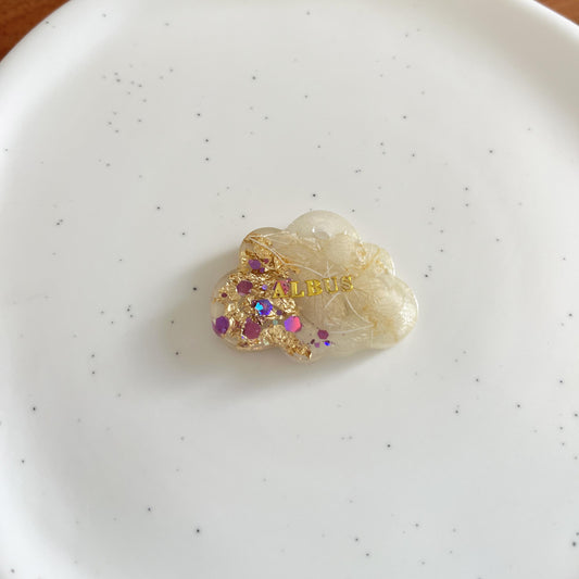 Médaille chien nuage en résine avec fleurs séchées, paillettes violettes et prénom doré, posée sur assiette blanche