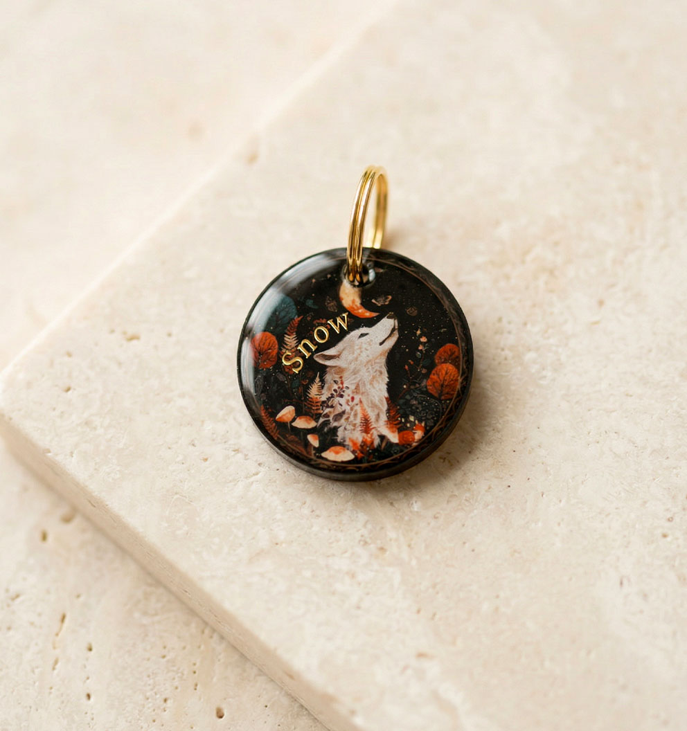 Médaille ronde personnalisée pour chien, design loup blanc hurlant sous la lune dans un décor de forêt d'automne. Le prénom Snow est inscrit en lettres dorées.