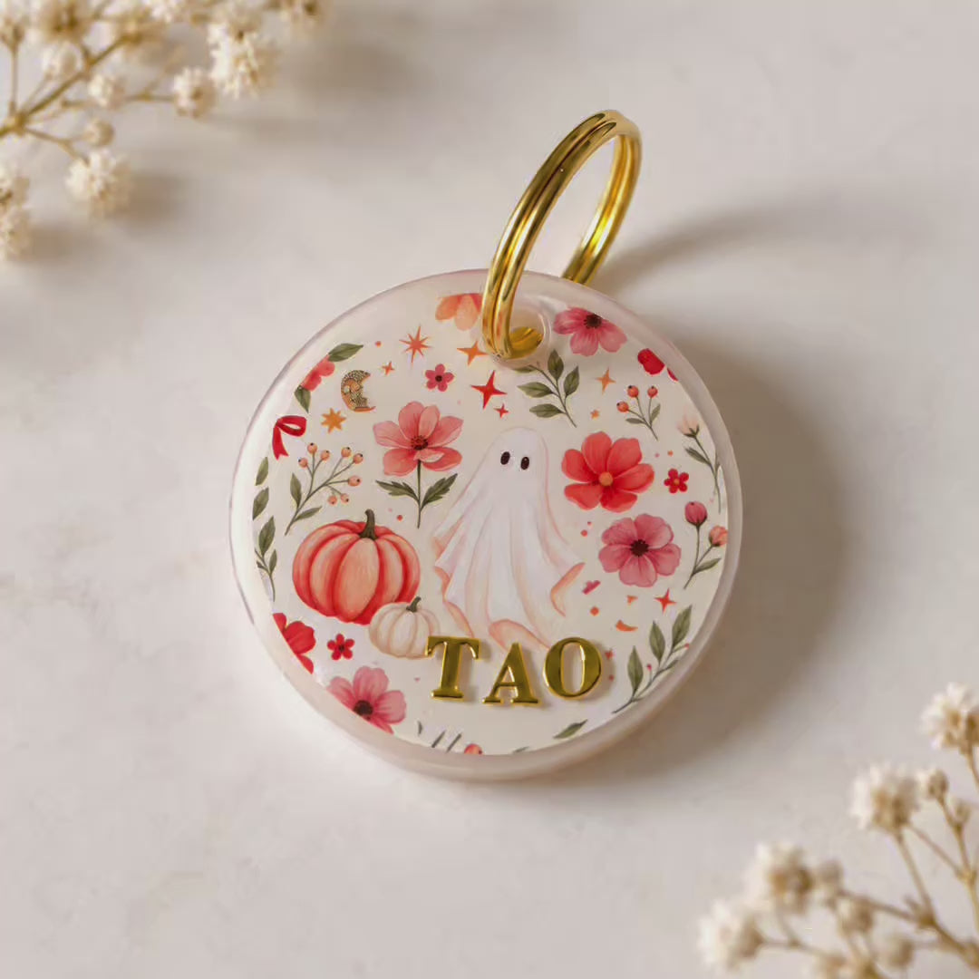 Vidéo de la médaille pour chien personnalisée Fantôme fleuri d’automne, en résine transparente avec fleurs, citrouilles et petit fantôme, personnalisée avec le prénom du chien en lettres dorées et présentée portée au collier.
